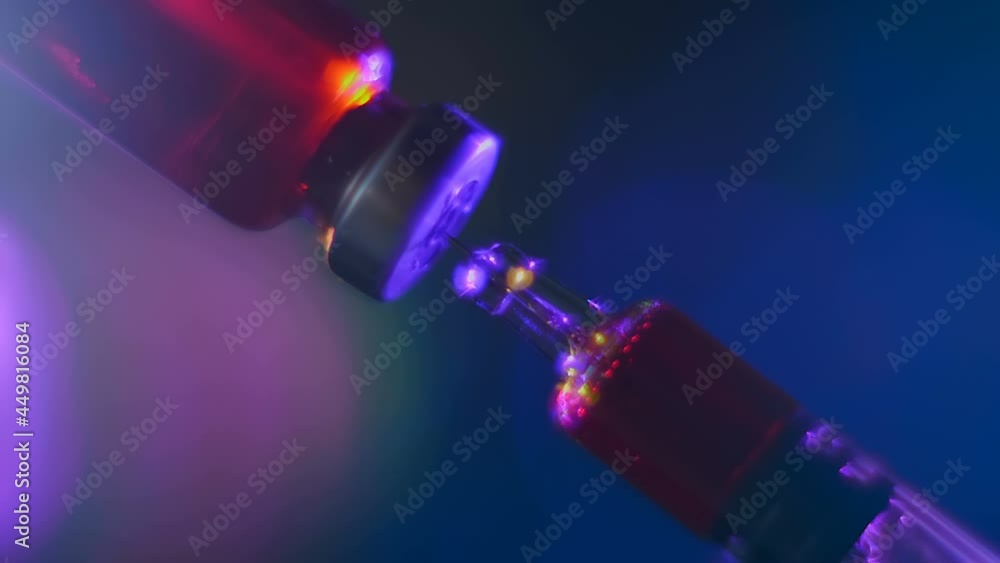 The needle of a glass modern syringe for vaccine injection takes medicine from a glass vial that glisten in color light on a colorful background. Closeup. Macro The needle of a glass modern syringe for vaccine injection takes medicine from a glass vial that glisten in color light on a colorful background. Closeup. Macro
