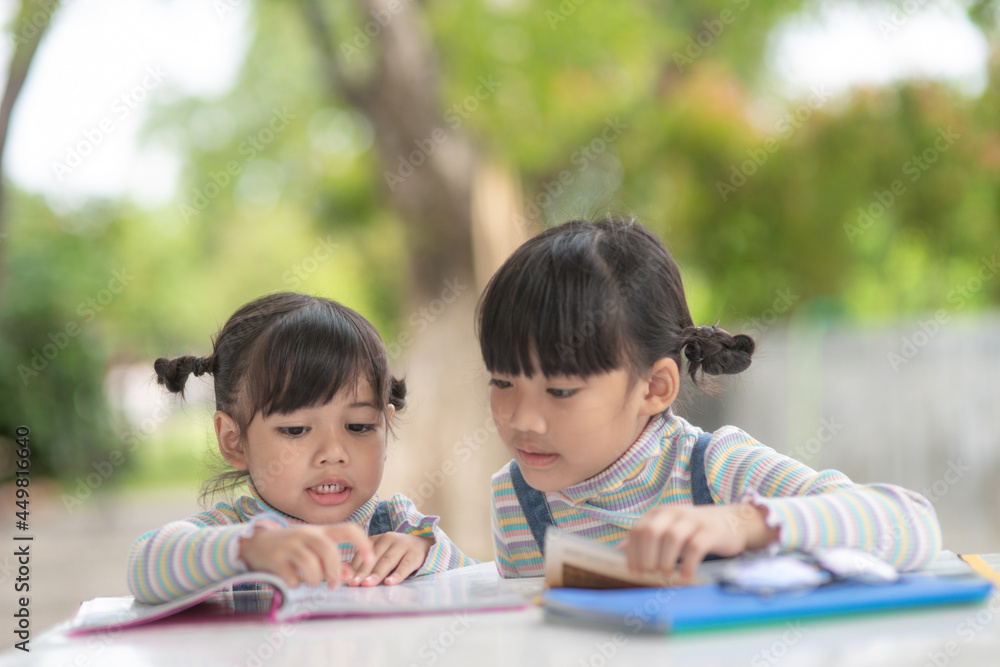Two student little Asian girls reading the book on table Two student little Asian girls reading the book on table
