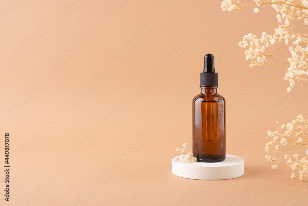 Amber glass dropper bottle with black lid on white podium for product presentation on beige background with dry plants. Skincare products ,natural cosmetic. Beauty concept for face and body care