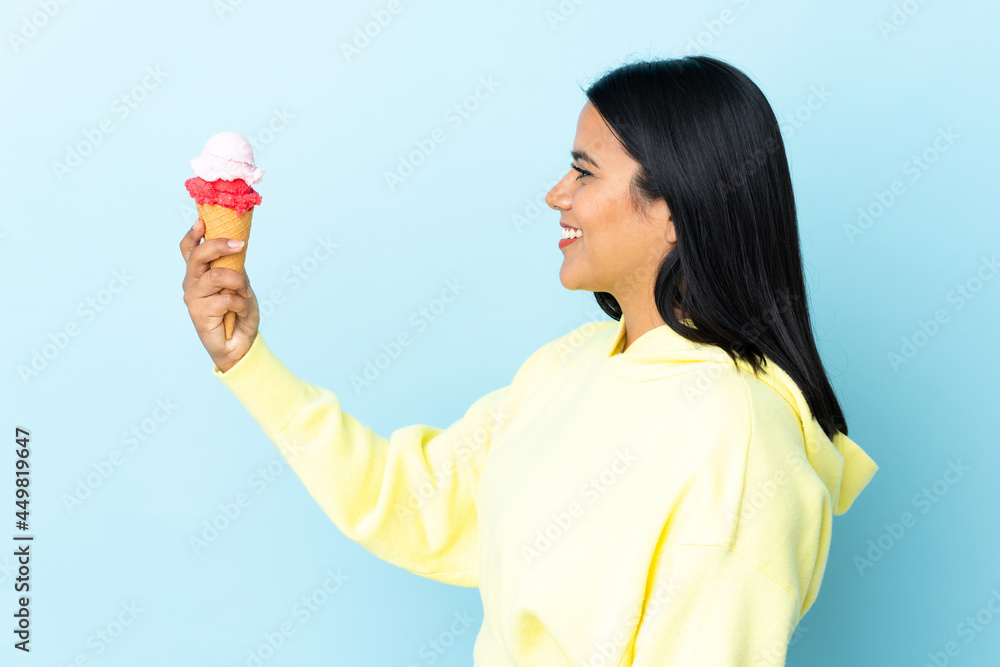 Young Colombian woman with a cornet ice cream isolated on blue background with happy expression Young Colombian woman with a cornet ice cream isolated on blue background with happy expression