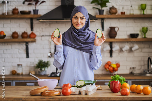 Pretty Muslim woman showing zucchini slices while cooking a meal