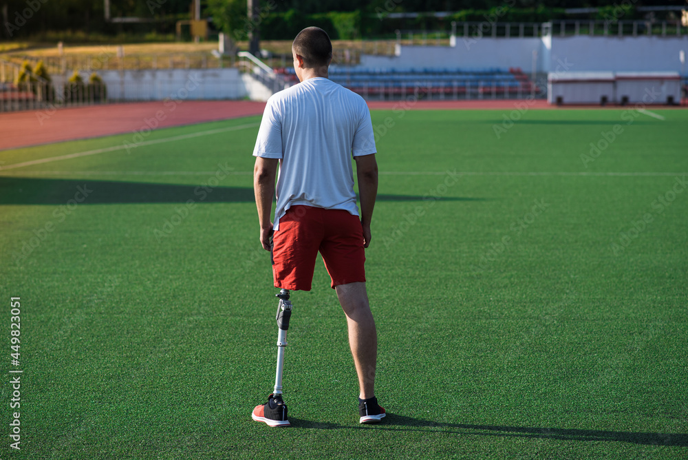 Portrait of young caucasian male athlete brunette with prosthetic leg on the stadium on the field. Back view. Portrait of young caucasian male athlete brunette with prosthetic leg on the stadium on the field. Back view.