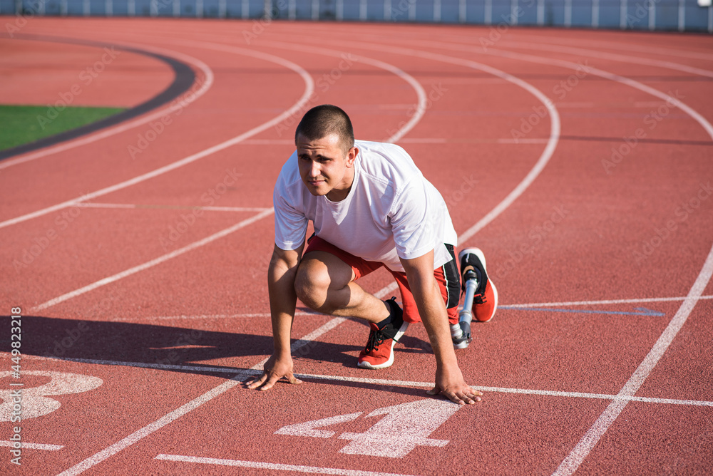 Obraz premium Caucasian male athlete with a prosthetic leg standing at the start on the track at the stadium. Sport concept.