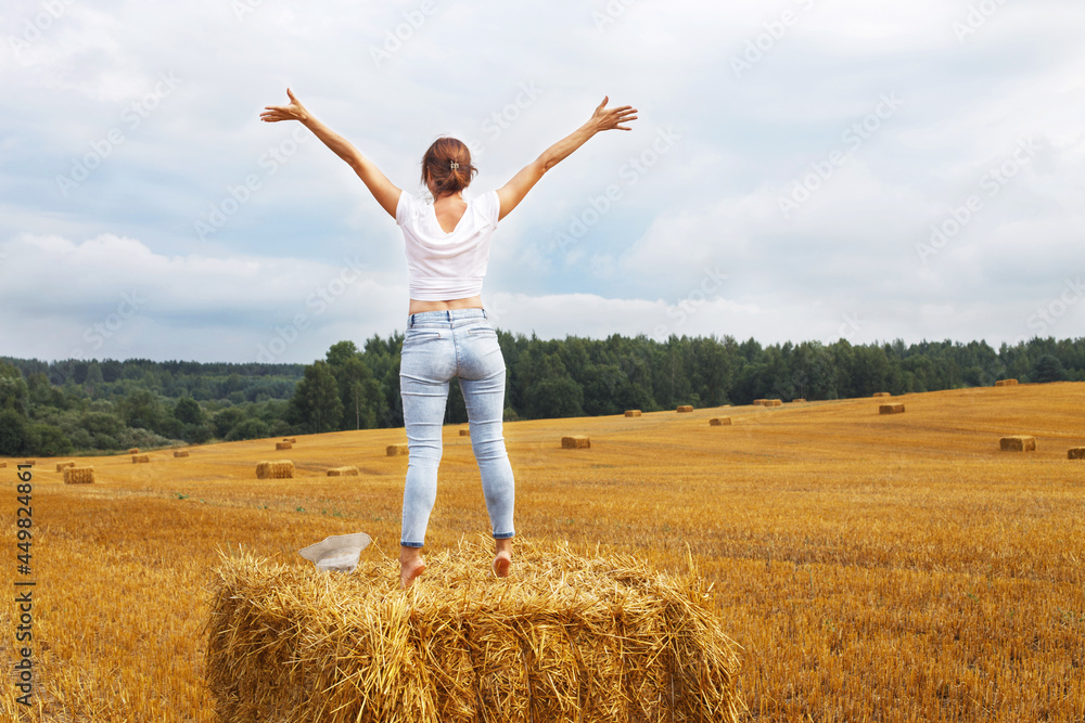girl with straw hat stands on a haystack on a bale in the agricultural field after harvesting girl with straw hat stands on a haystack on a bale in the agricultural field after harvesting