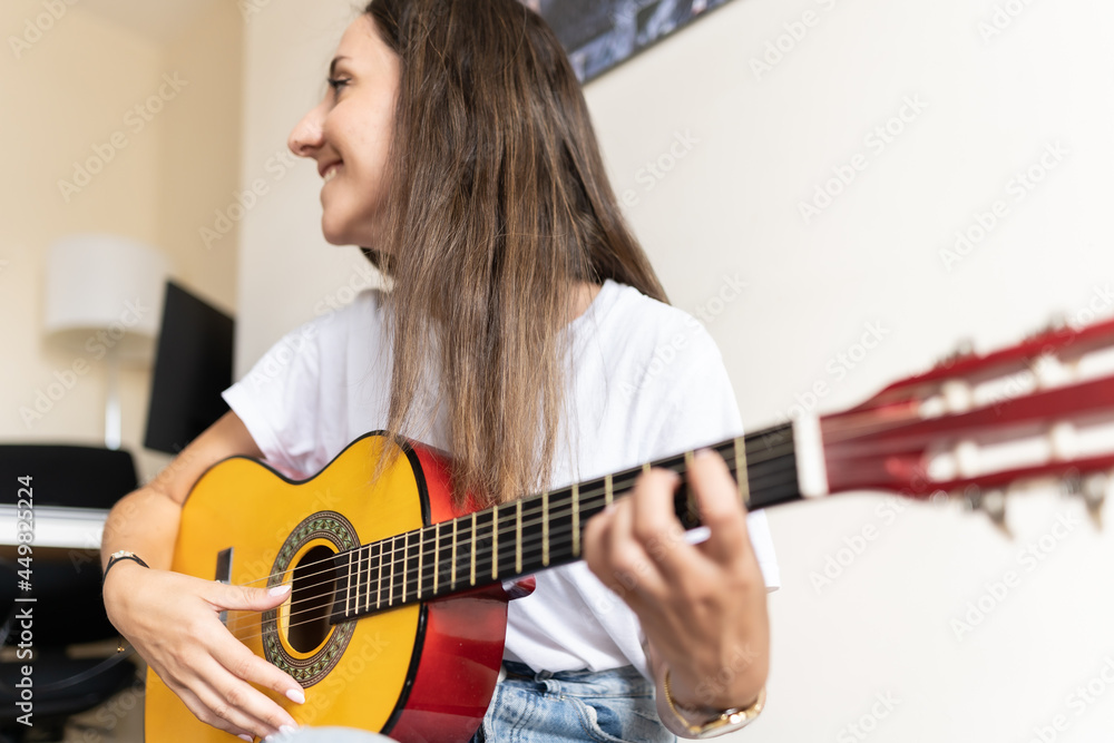 Fototapeta premium Attractive young female smiling while playing the guitar at home while learning new chords and practising new songs