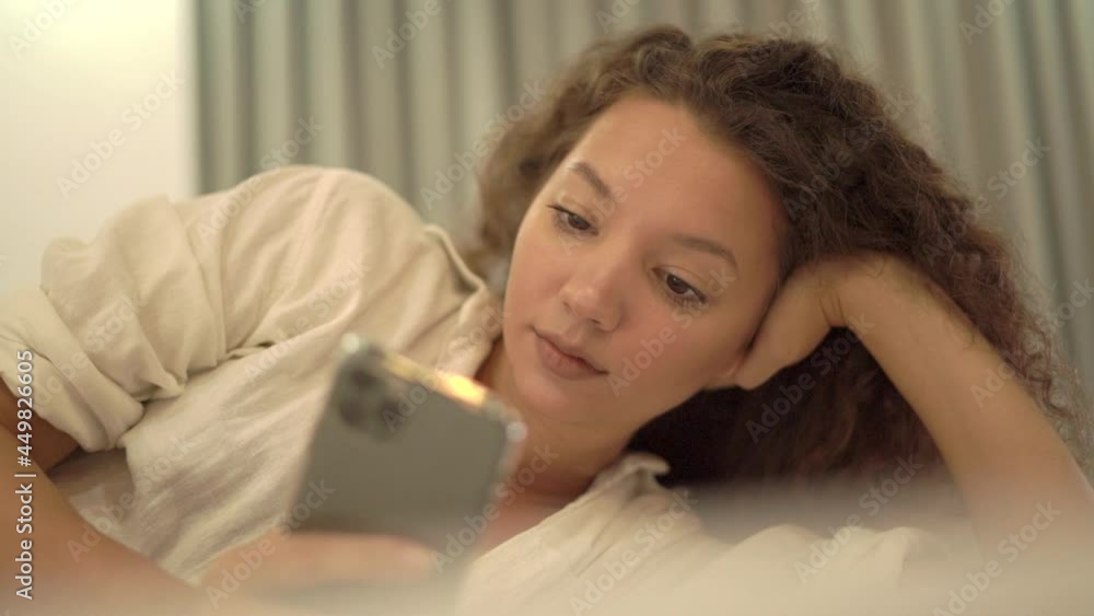 Relaxed mixed race lady reads article on contemporary smartphone. Young woman lies on bed enjoying lazy evening close view. Concept leisure pastime Relaxed mixed race lady reads article on contemporary smartphone. Young woman lies on bed enjoying lazy evening close view. Concept leisure pastime