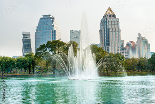 Beautiful lake with fountain in green Lumphini park and skyscrapers buildings on skyline. Bangkok city, Thailand