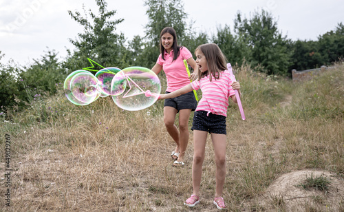 Little girl and mom are playing with big soap bubbles in nature.