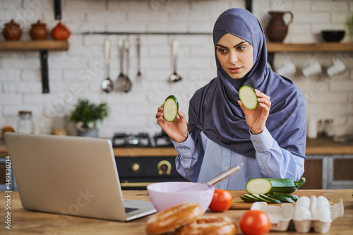 Young Arabian woman having a video call and showing slices of zucchini