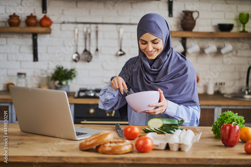 Arabian woman cooking a meal and having a video call on a laptop