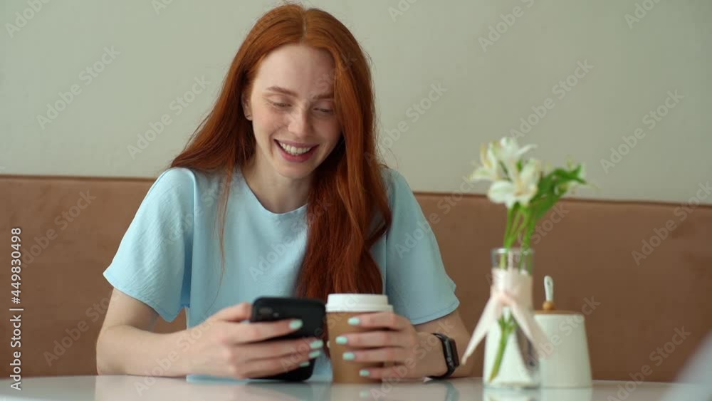 Front view of happy young Caucasian woman using smartphone chatting with friends and drinking hot coffee sitting at table in cozy cafe. Portrait of cheerful female using app on phone in coffee shop. Front view of happy young Caucasian woman using smartphone chatting with friends and drinking hot coffee sitting at table in cozy cafe. Portrait of cheerful female using app on phone in coffee shop.