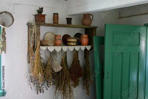 An interior of an old rural hose with all the neccesary items located on shelves, including brooms, pots, cauldrons, cuttlery, and bowls see next to green wooden door on a sunny summer day in Poland photo