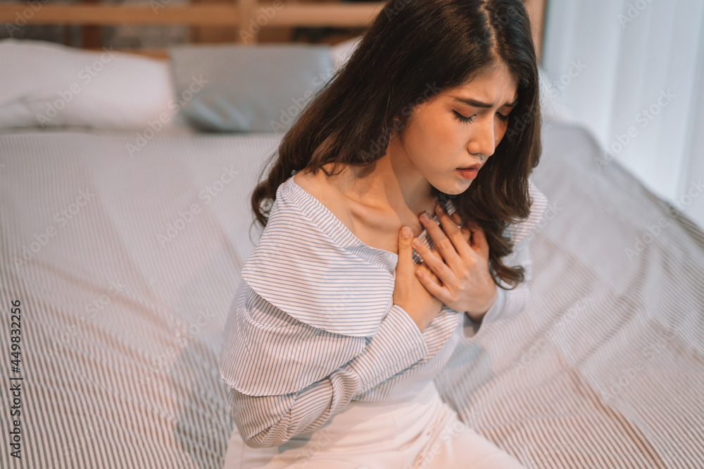 Portrait of 20s young Asian woman having difficulty breathing in bedroom at night. Shortness of breath, asthma, difficult to breathe problems. Corona Virus symptoms.