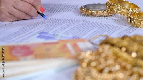 Female signing gold loan agreement against her gold jewelry - financial planning. Indian bank currency notes and some jewelry kept together - financial security