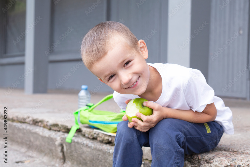 a boy of European appearance with a green apple in his hands sits on the porch of the school
a boy of European appearance with a green apple in his hands sits on the porch of the school