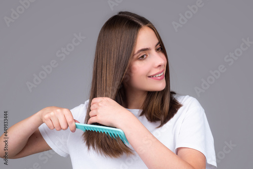 Portrait of beautiful young woman combing her hair, smiling. Female brushing healthy hair with comb.
