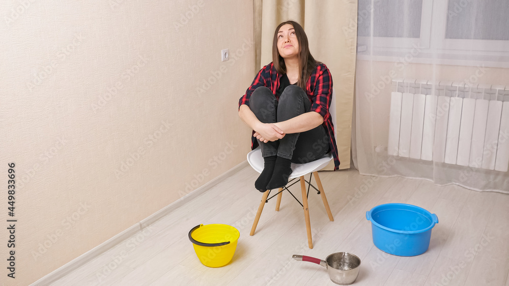 Water damage. Upset woman sits on chair near containers in light living room. water drips from the ceiling in the apartment. Concept of flooding the apartment and property insurance Water damage. Upset woman sits on chair near containers in light living room. water drips from the ceiling in the apartment. Concept of flooding the apartment and property insurance