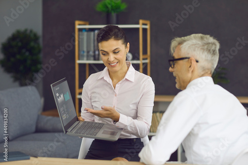 Smiling bank agent or financial company expert meeting client in office, showing percentage figures on laptop screen, explaining business deal details, offering loan or fixed deposit with good returns