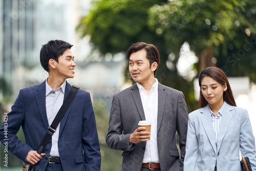 three asian business people commuting in modern city walking talking on street