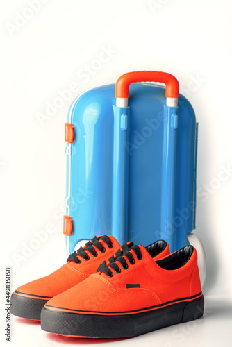 Blue suitcase and orange gumshoes on white background. Travel concept. Copy space.