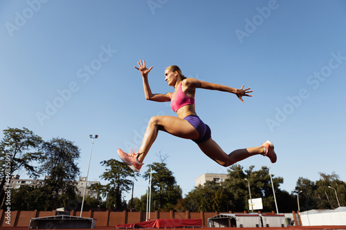 One Caucasian woman, female athlete, runner training at public stadium, sport court or palyground outdoors. Summer sport games. © master1305
