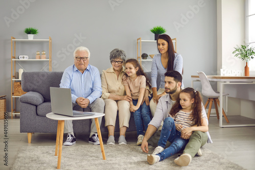 Grandparents, young couple and their daughters spend time together. Large friendly family gathered together at home in the living room to watch a movie on a laptop. Family concept.