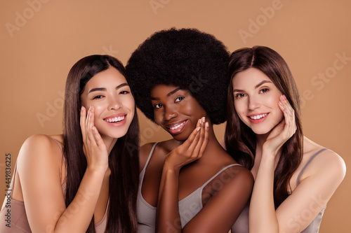 Photo of cute sweet three best friends wear cropped tops embracing arms cheeks smiling isolated beige color background