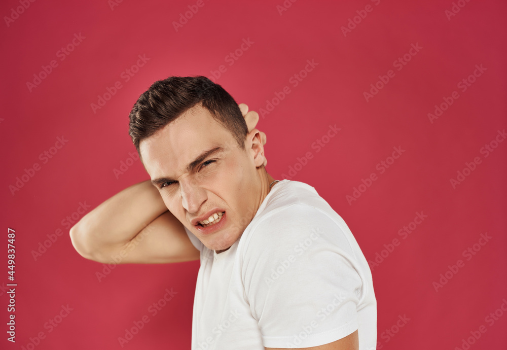 a man with an angry expression holds his hand behind his head white t-shirt Studio red background a man with an angry expression holds his hand behind his head white t-shirt Studio red background