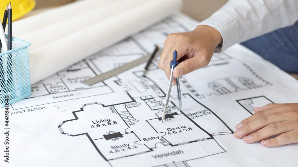 Young man structural design or engineer is using a measuring circle around a floor plan or blueprint, Architect or engineer is designing a building using compasses to draw the physical structure. Young man structural design or engineer is using a measuring circle around a floor plan or blueprint, Architect or engineer is designing a building using compasses to draw the physical structure.