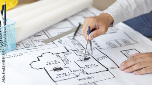 Young man structural design or engineer is using a measuring circle around a floor plan or blueprint, Architect or engineer is designing a building using compasses to draw the physical structure.