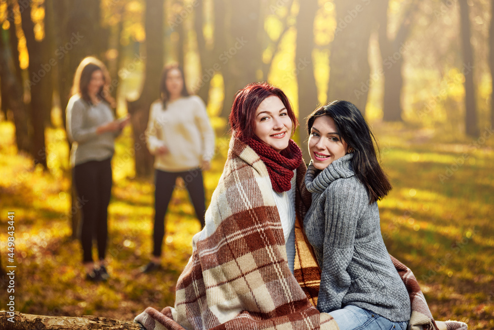 Attractive smiling women posing in forest on warm day, two female friends on the background