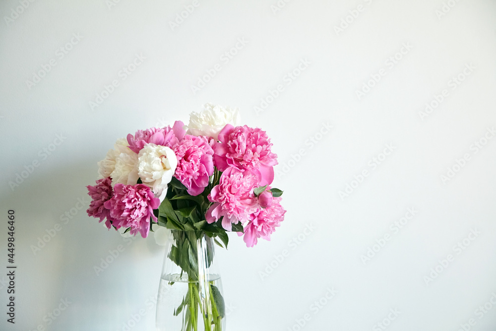 Empty white wall with pink flowers. Peonies in a glass vase in a bright interior