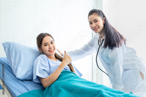 Asian young female patient on bed showing thumbs up with smiley face very good symptom to asian young female nurse doctor in hospital background.