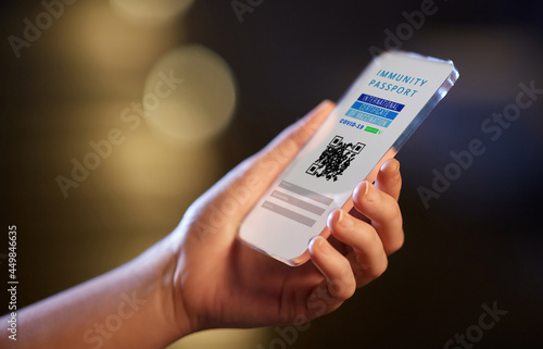 technology and health care concept - woman's hand holding transparent smartphone with virtual immunity passport or international certificate of vaccination on screen over dark background