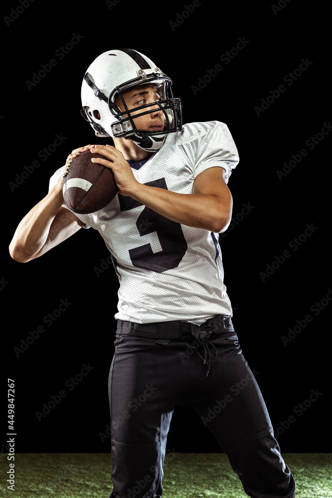 One professional American football player playing football isolated on dark studio background with green grass flooring. Concept of sport, competition One professional American football player playing football isolated on dark studio background with green grass flooring. Concept of sport, competition