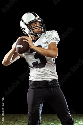 One professional American football player playing football isolated on dark studio background with green grass flooring. Concept of sport, competition