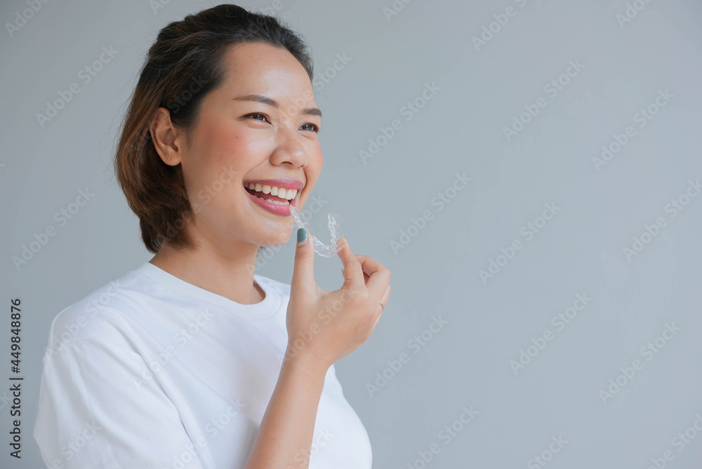close up young asian woman smiling with hand holding dental aligner retainer (invisible) on gray background of dental clinic for beautiful teeth treatment course concept close up young asian woman smiling with hand holding dental aligner retainer (invisible) on gray background of dental clinic for beautiful teeth treatment course concept
