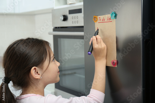 Fotografia Little girl writing to do list on fridge in kitchen