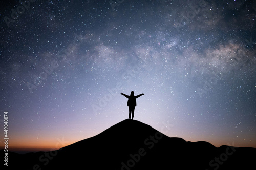 Silhouette of young female with backpack standing and raise both hands watched the star and milky way alone on top of the mountain. She enjoyed traveling and was successful when he reached the summit.