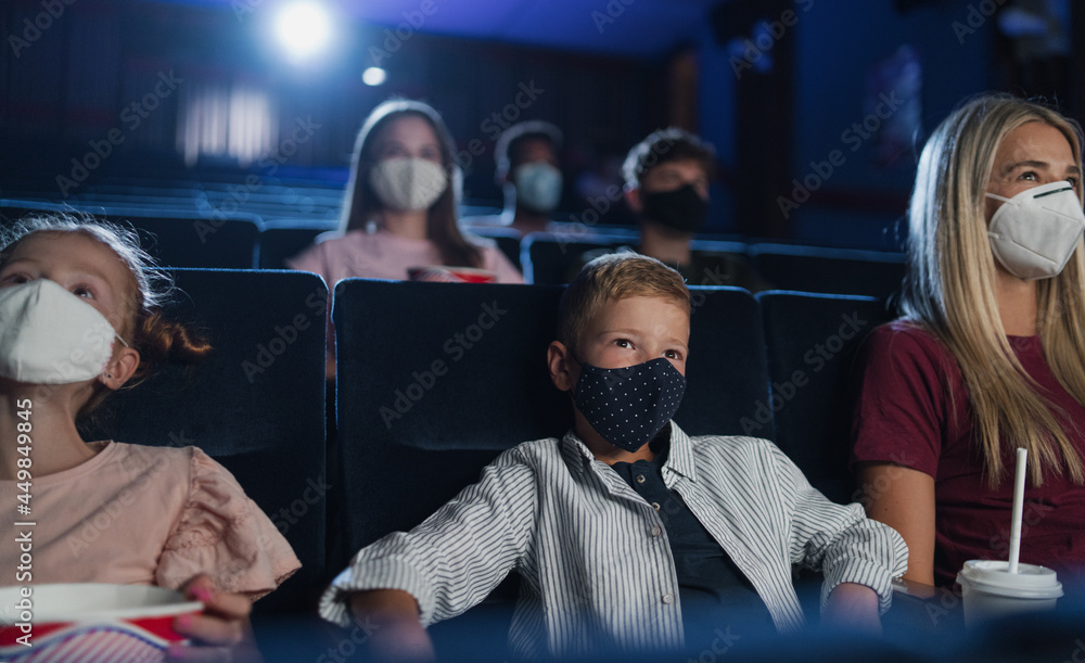 Mother with happy small children watching film in the cinema, coronavirus concept.