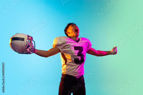 Portrait of American football player training isolated on blue studio background in neon light. Concept of sport, competition