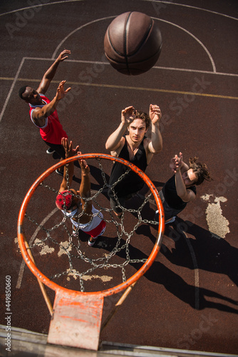 Overhead view of man throwing basketball ball near multiethnic friends with raised hands and hoop