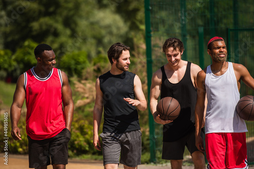 Interracial sportsmen with basketball balls walking outdoors