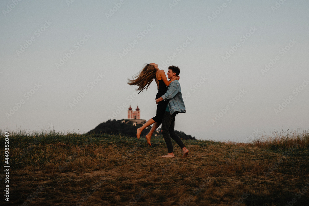 Young couple on a walk in nature at dusk in countryside, having fun hugging.