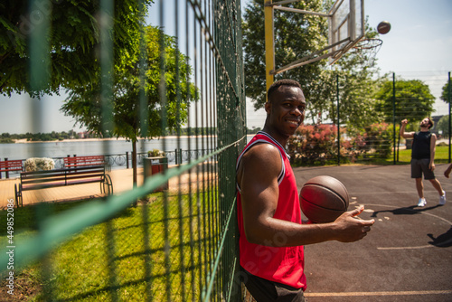 Young african american sportsman holding basketball ball near blurred fence on playground © LIGHTFIELD STUDIOS