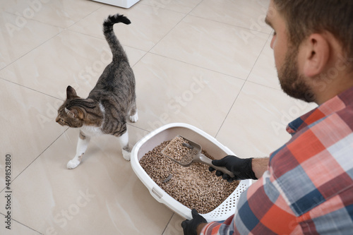 Young man in gloves cleaning cat litter tray at home