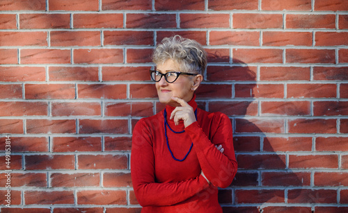 Senior woman standing outdoors against brick wall background. Copy space.