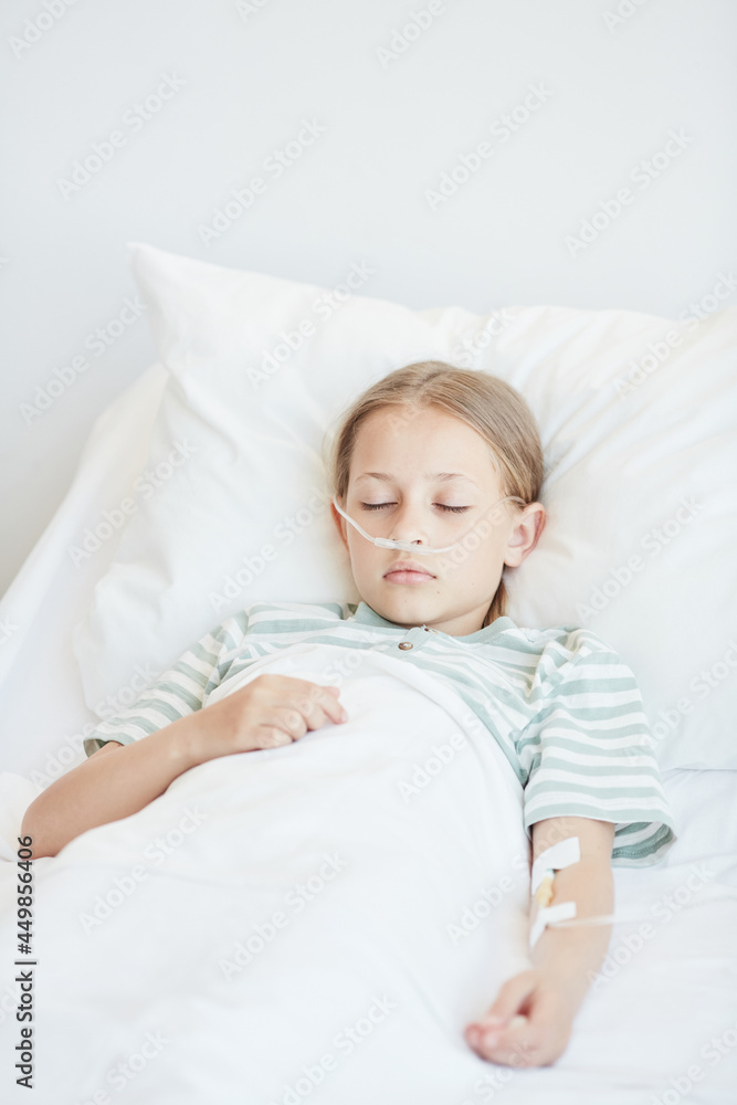 Vertical portrait of little girl laying in hospital bed with oxygen support and IV drip