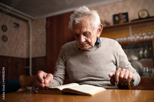 Portrait of elderly man sitting at the table indoors at home, reading book.