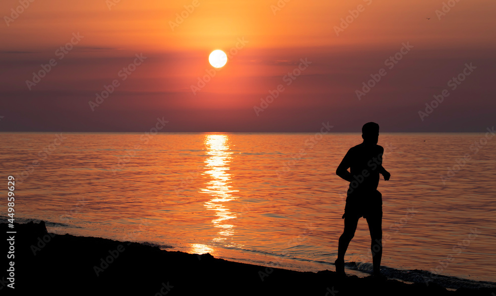 Silhouette of the man who is running in the sunrise rays on the sea.